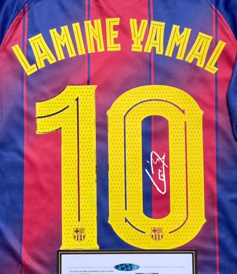 May include: A close-up of a blue, red, and yellow soccer jersey. The jersey features the name "LAMINE YAMAL" in yellow lettering across the back, with the number "10" in yellow. A signature is visible on the number. The FC Barcelona crest is present.