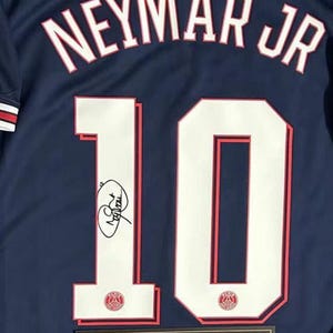 May include: Navy blue jersey with the name "NEYMAR JR" arched across the back in white lettering. The number "10" is prominently displayed in white with red trim. Includes a signature and a certificate of authenticity.