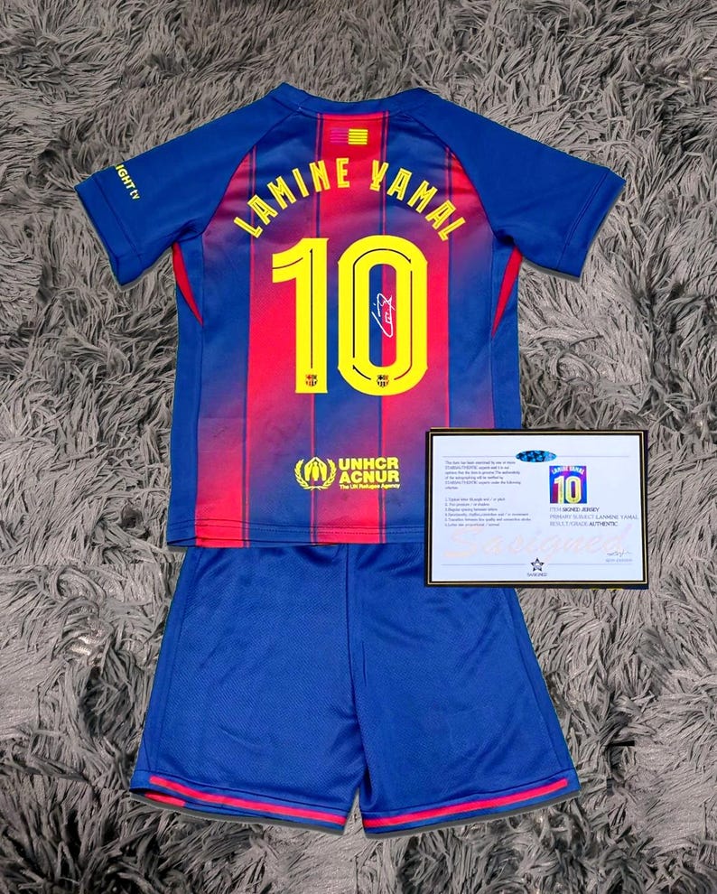 May include: A blue and red soccer jersey and shorts set. The jersey features the name "LAMINE YAMAL" and the number "10" in yellow. The set includes a certificate of authenticity.