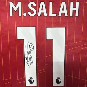 May include: A red soccer jersey with the name "M. SALAH" and the number "11" on the back. The number is signed with a doodle of a person.