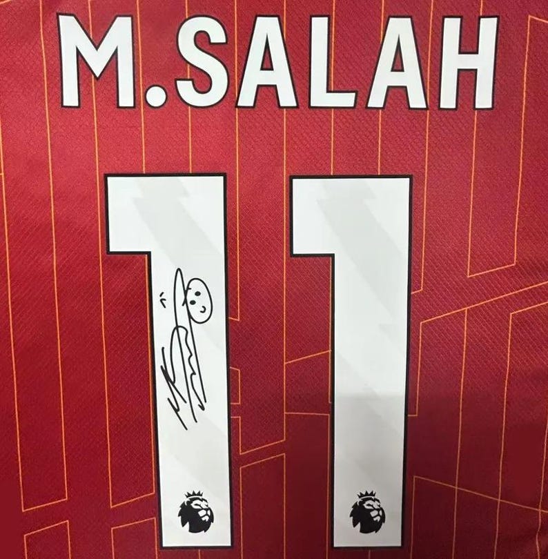 May include: A red soccer jersey with the name "M. SALAH" and the number "11" on the back. The number is signed with a doodle of a person.