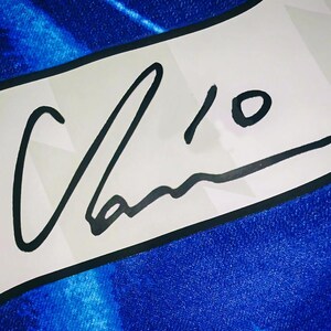 May include: A white banner with a black border displays a signature and the number 10 in black ink. The banner is set against a textured blue background, creating a contrast between the white and blue.