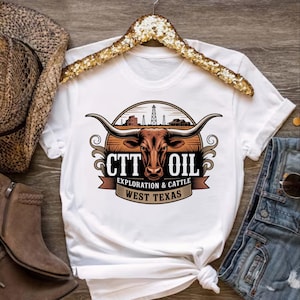 May include: White t-shirt featuring a graphic with a longhorn, oil derricks, and the text "CTT OIL EXPLORATION & CATTLE WEST TEXAS." The design is in shades of brown, tan, and black. The shirt is displayed on a wooden surface.