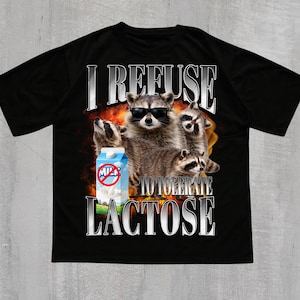 Op de afbeelding: Zwart T-shirt met een afbeelding van wasberen met een zonnebril en een melkpak. De tekst op het shirt luidt "I REFUSE TO TOLERATE LACTOSE". Het woord "BLACK" staat onderaan het shirt.