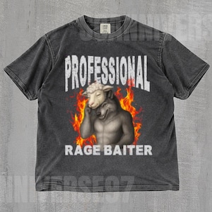 Peut inclure: T-shirt gris foncé avec les mots "PROFESSIONAL RAGE BAITER" en blanc. Le graphisme représente une tête de mouton sur un corps de loup avec des flammes. Le t-shirt est en matière souple.