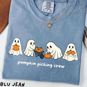 Può includere: T-shirt blu con una grafica di quattro fantasmi dei cartoni animati con zucche e la scritta "pumpkin picking crew". La maglietta è del marchio Comfort Colors e ha una collana d'oro.