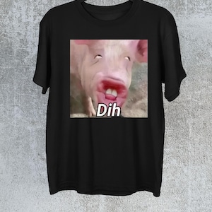 Könnte beinhalten: Schwarzes T-Shirt mit einem Nahaufnahmen-Bild eines Schweinegesichts, offenem Mund und dem Wort "Dih" in Weiß. Das Schwein hat rosa Haut und sichtbare Zähne. Das T-Shirt hängt an einem schwarzen Kleiderbügel.