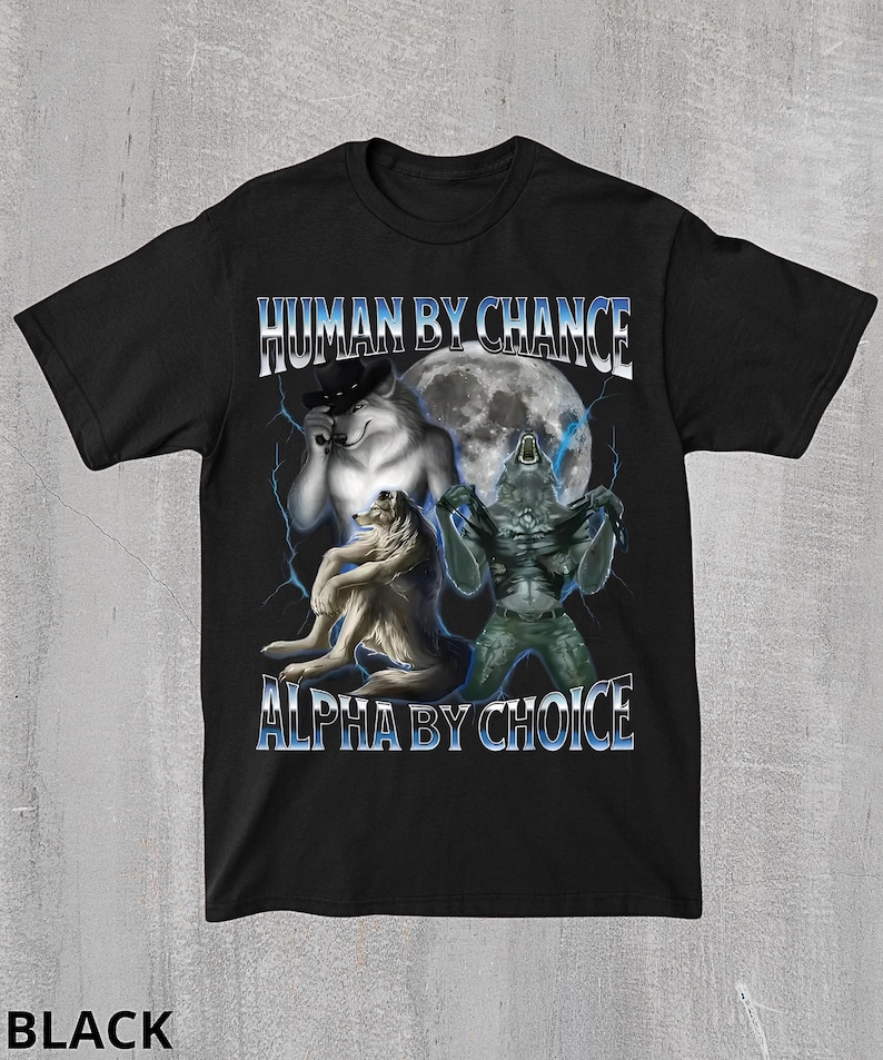May include: Black t-shirt featuring a graphic design with three wolf-like creatures in front of a full moon. The text "HUMAN BY CHANCE" and "ALPHA BY CHOICE" are displayed in a blue and white font.