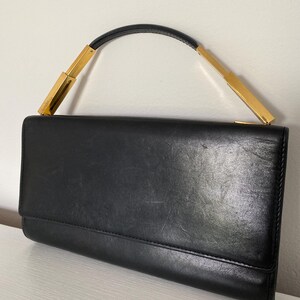 A black leather clutch with a gold metal handle. The clutch has a flap closure and a smooth, textured surface.