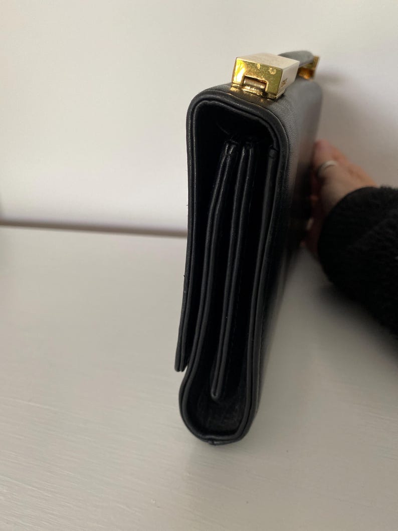 May include: Black leather briefcase with a gold-toned clasp. The briefcase has a rectangular shape with a structured design. The clasp is rectangular and has a gold finish. The briefcase is closed.