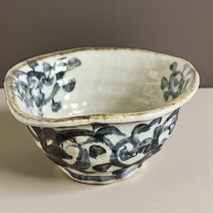 Peut inclure: Un bol en céramique avec un intérieur blanc et un motif floral bleu foncé. Le bord et l'extérieur du bol ont une finition texturée, brun clair. Le bol a une forme carrée légèrement irrégulière.