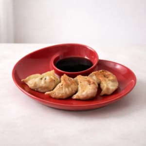 May include: A red ceramic plate with a built-in sauce bowl holds four golden-brown dumplings. The bowl is filled with dark sauce. The dumplings are arranged on the plate, ready to be enjoyed.