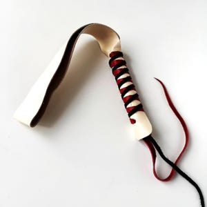 May include: A white leather whip with a red and black braided handle.