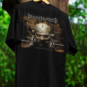 Puede incluir: Camiseta negra con el nombre de la banda "DECAPITATED" en letras góticas blancas. El gráfico muestra una figura con forma de calavera con ojos rojos. El texto "ORGANIC HALLUCINOSIS" está impreso debajo.