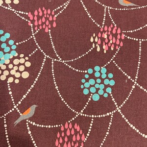 May include: A brown fabric with a repeating pattern of white dots, teal and pink circles, and small pink teardrop shapes. Two small brown birds are perched on the fabric.