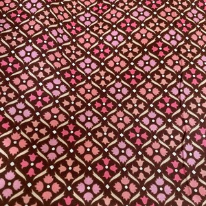 May include: A brown fabric with a repeating pattern of pink and white flowers. The flowers are arranged in a diamond pattern.