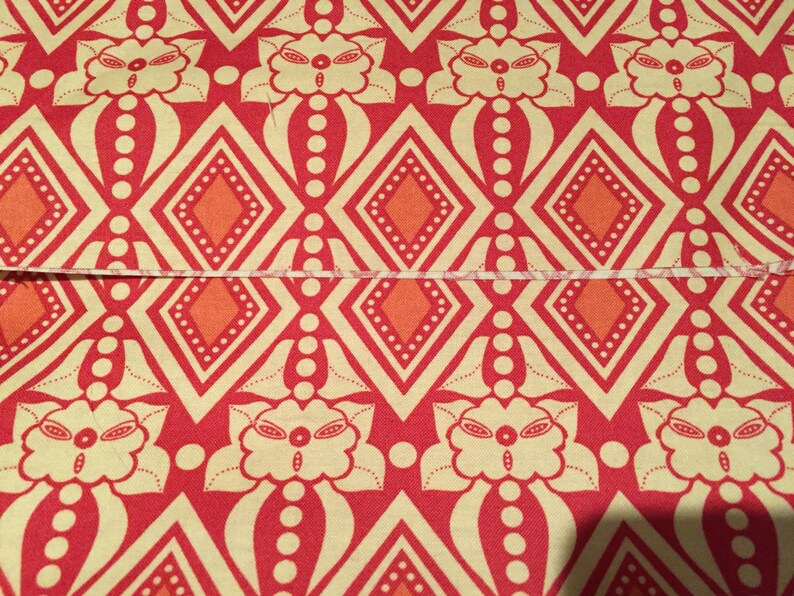 May include: Red fabric with a repeating pattern of white stylized flowers, orange diamonds, and white dots.