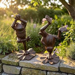Peut inclure: Deux sculptures de grenouilles en métal brun foncé texturé, posées sur des socles en forme de nénuphar. Une grenouille est en équilibre sur une patte, bras levés, tandis que l'autre fait le poirier, une patte en l'air, sur un muret.