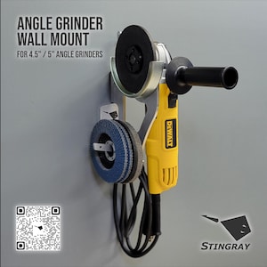 May include: A yellow and black angle grinder with a black handle is mounted on a gray wall. The grinder is held by a silver metal bracket. The text "ANGLE GRINDER WALL MOUNT" is visible. A blue grinding disc is also mounted.