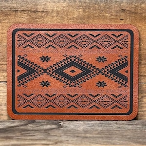 May include: A brown leather coaster with a black geometric pattern. The pattern is a repeating design of diamonds and triangles.