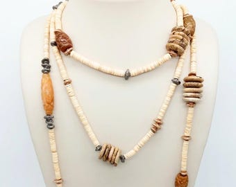 May include: Three layered necklace with cream-colored disc beads, accented with brown and tan carved beads and silver-toned metal spacers. The necklace is displayed on a white mannequin.