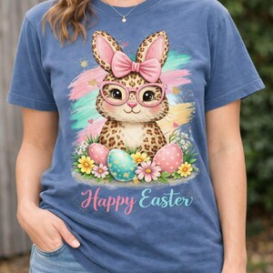 以下が含まれることがあります： イースターをテーマにした青いTシャツ。ヒョウ柄のウサギがメガネとピンクのリボンを着用したデザイン。カラフルなイースターエッグと「Happy Easter」の文字も表示されています。