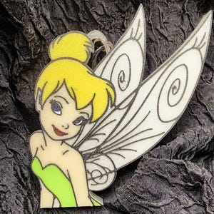 May include: A colorful cartoon image of a fairy with yellow hair, blue eyes, and a green dress. The fairy has large white wings with black outlines. The image is set against a dark, textured background.