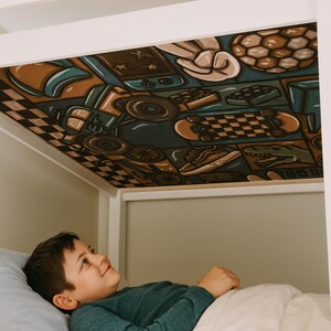 May include: A child's bed with a colorful, patterned canopy featuring illustrations of skateboards, sports equipment, and other objects. The bed frame is white, and the child is lying in bed looking up at the canopy.