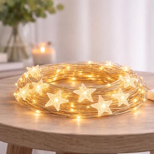 Op de afbeelding: Een opgerolde lichtslinger met warmwitte LED's en stervormige accenten. De lichten zijn gerangschikt op een houten tafel, met een witte bedieningsbox in de buurt. Decoratie voor in huis.