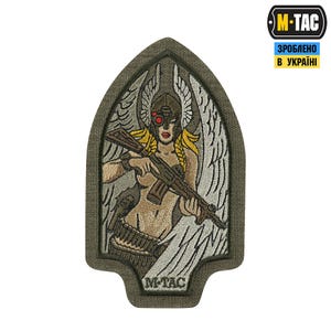 Könnte beinhalten: Gestickter Aufnäher mit einer geflügelten Figur, die ein Gewehr hält und einen Helm mit rotem Augenschutz trägt. Die Figur hat blonde Zöpfe und ist vor einem weißen Hintergrund in einem grünen Rahmen platziert. Der Aufnäher trägt den Text "M-TAC".