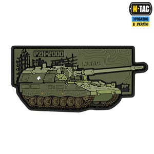 Puede incluir: Un parche verde oliva con una ilustración detallada de un tanque obús autopropulsado PZH-2000. El parche incluye el texto "PZH-2000" y "M-TAC", con un símbolo de cruz blanca. El fondo es verde oliva texturizado.
