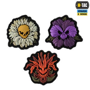 May include: Three embroidered patches with floral designs and skull faces. One patch features a daisy with a yellow skull center. Another shows a purple pansy with a skull. The third patch has an orange and red flower with a skull face.