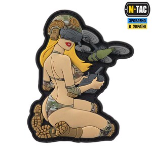 Puede incluir: Un parche que representa a una mujer de dibujos animados con un bikini y casco de camuflaje, operando un dron. La mujer tiene el pelo rubio y lápiz labial rojo. El parche tiene el texto "M-TAC" y "Hecho en Ucrania".