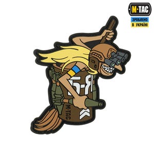 Puede incluir: Un parche de dibujos animados que presenta un personaje con cabello rubio, que lleva un casco marrón con binoculares y sostiene una escoba y una botella. El personaje está montado en una mochila marrón con el texto "5-9" y "M-TAC".