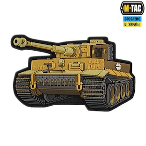 Op de afbeelding: Een bruine en gele plastic patch met daarop een Duitse Tiger-tank uit de Tweede Wereldoorlog met de tekst "Real Tiger" aan de zijkant. De patch is gelabeld met "M-Tac" en "ЗРОБЛЕНО В УКРАЇНІ", wat "Gemaakt in Oekraïne" betekent.