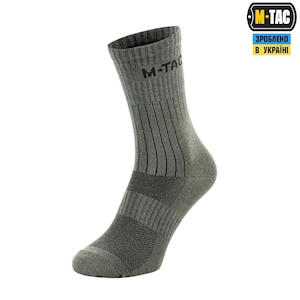 May include: A single olive green M-TAC sock. The sock features vertical ribbed detailing along the leg and a reinforced heel and toe. The M-TAC logo is printed in black near the top of the sock.