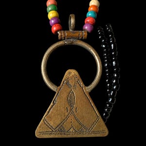May include: A necklace featuring a triangular brass pendant with etched geometric patterns suspended from a circular brass ring. The necklace includes a strand of multicolored beads in red, green, yellow, purple, and orange, alongside black beads.