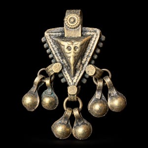 May include: A triangular brass pendant with an aged finish, featuring a central embossed design and a top loop. Six small, rounded bell-like charms are suspended from the base and sides of the triangle by small metal rings, creating a layered look.
