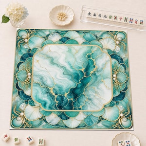 May include: A square mahjong mat featuring a central teal and white marble pattern with gold veining, surrounded by a border of scalloped shell motifs, gold coral accents, and white pearls, with a gold-toned frame around the center design.