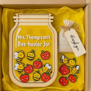 May include: A wooden jar-shaped sign with the text "Mrs. Thompson's Bee-havior Jar" and bee and apple cutouts. Includes a small bag with a "Thank you" tag, all inside a box with yellow tissue paper.