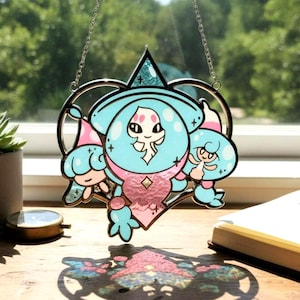 Puede incluir: Un atrapasoles de vidriera con un personaje de dibujos animados caprichoso en tonos azul claro y rosa. El personaje tiene una cabeza grande y está rodeado por un marco en forma de corazón. El atrapasoles cuelga de una cadena plateada.