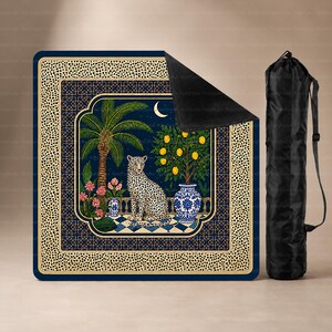 Peut inclure: Une couverture d'extérieur carrée ornée d'un léopard sur une terrasse carrelée avec un palmier, un citronnier dans un vase bleu et blanc, et un croissant de lune. La bordure présente un motif léopard. Un sac de transport noir est inclus.