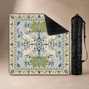May include: A rectangular picnic blanket featuring a symmetrical pattern of four white tigers, green palm leaves, and small birds on a light blue background with a decorative border, accompanied by a black cylindrical carrying bag with a shoulder strap.