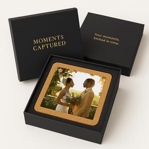 May include: A black box with the words "Moments Captured" in gold lettering. The box contains a cork coaster with a photo of a couple in a wedding setting. The text "Your moments. Etched in time." is printed on the top of the box.