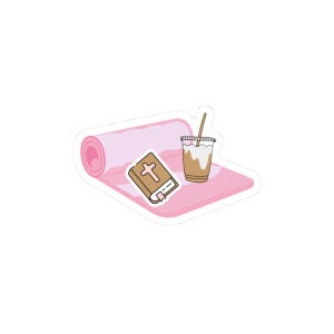 Puede incluir: Una esterilla de yoga rosa con un libro marrón que presenta una cruz blanca en la portada y un vaso de plástico transparente lleno de café helado marrón claro con una pajita, todo ilustrado como una pegatina con borde blanco.