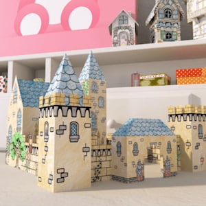 Könnte beinhalten: Ein detailliertes, handgezeichnetes Papier-Schloss mit blauen und gelben Akzenten. Das Schloss verfügt über mehrere Türme, Türmchen und ein Tor mit einem skurrilen Design. Andere Miniatur-Papierhäuser befinden sich auf einem Regal im Hintergrund.