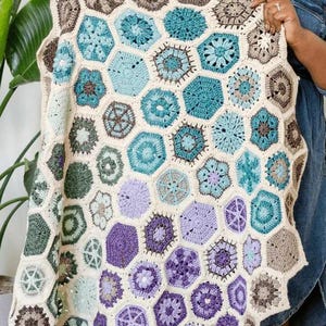 May include: A handmade crochet blanket featuring a geometric pattern of interconnected hexagons. The blanket showcases a palette of cream, teal, purple, and brown hues. The intricate design and color scheme create a visually appealing and cozy textile.