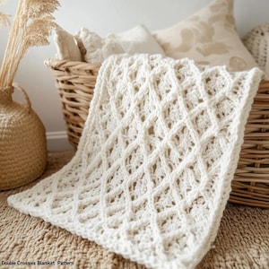 May include: A cream-coloured, crocheted blanket with a diamond pattern, draped over a wicker basket. The blanket's texture is visible, and the design is intricate. The words "Double Crosses Blanket Pattern" are at the bottom of the image. The blanket is on a neutral-toned rug.
