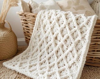 May include: Cream-colored, crocheted blanket with a diamond pattern, draped over a woven basket. The blanket's texture is visible, and the design is intricate. The words "Double Crosses Blanket Pattern" are at the bottom of the image. The blanket is on a neutral-toned rug.