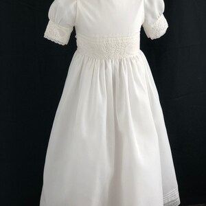 May include: White dress with lace trim and puffed sleeves. The dress has a round neckline and a full skirt.
